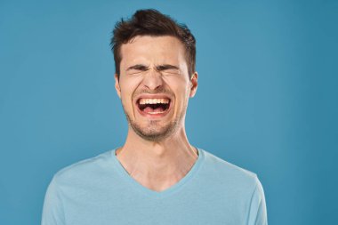 Stüdyoda mavi arka planda bağıran genç yakışıklı adam. 