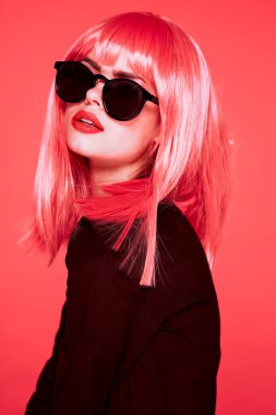 Pembe peruklu ve pembe arka planda güneş gözlüklü güzel bir kadın.