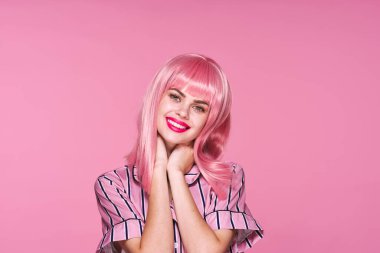 Pembe peruklu genç bir kadın pembe arka planda poz veriyor.