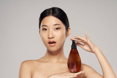 Stüdyoda saç spreyi olan genç, güzel Asyalı kadın izole edilmiş arka planda.