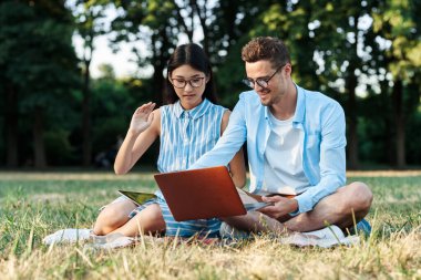 Dizüstü bilgisayarı olan genç öğrenciler çimlerin üzerinde oturuyor. 