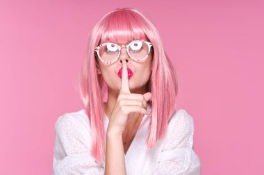 Pembe peruklu genç bir kadın. Pembe arka planda sessizlik jesti.