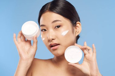 Stüdyoda krem tutan genç, güzel Asyalı bir kadın.