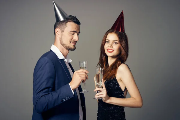 Young beautiful couple in party hats celebrating New year  with champagne  grey on background