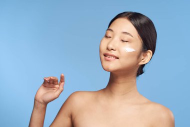 Güzel Asyalı bir kadının portresi izole edilmiş arka planda krem sürüyor.