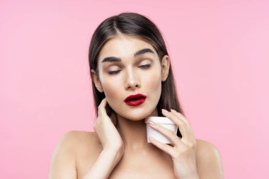 Güzel bir kadının portresi pembe arka planda güzellik ürünü taşıyor.