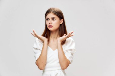 Gri arka planının önünde, yüzünü buruşturan bir kadın var. 