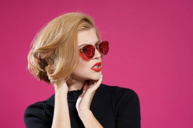 Koyu renk gözlüklü, parlak makyajlı, siyah ceketli, yakın plan pembe arka planlı güzel bir kadın.
