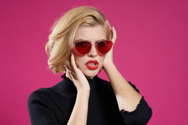 Koyu renk gözlüklü, parlak makyajlı, siyah ceketli, yakın plan pembe arka planlı güzel bir kadın.