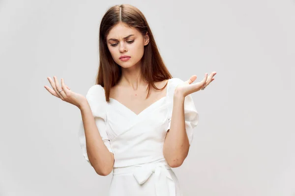 Woman with displeased expression looking down holding hands in front of her white dress gray — Stock Photo, Image