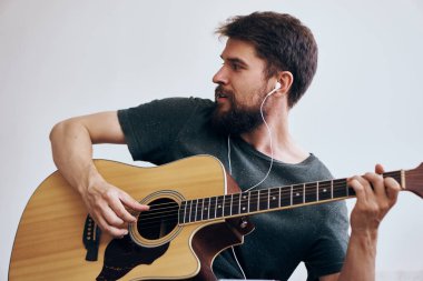 Gitar çalan bir adam müzik öğreniyor. Koyu renk tişörtlü açık arka plan.