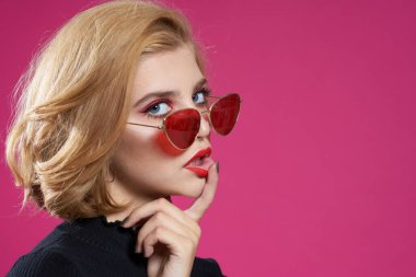 Koyu renk gözlüklü, parlak makyajlı, siyah ceketli, yakın plan pembe arka planlı güzel bir kadın.