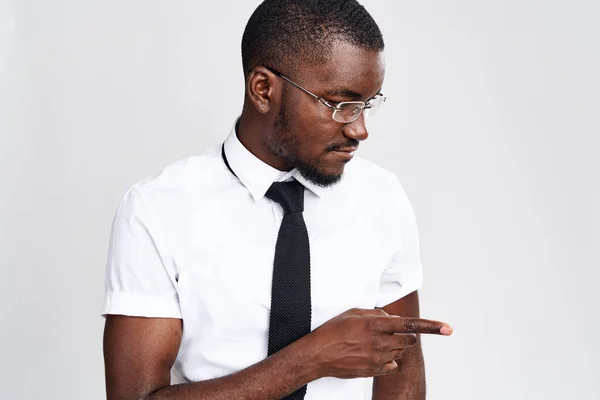 Um homem africano com uma camisa e gravata em um fundo leve gestos com as mãos Copiar espaço — Fotografia de Stock