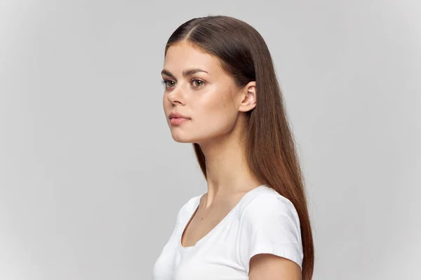 Donna su uno sfondo grigio in una t-shirt bianca guarda a lato — Foto Stock