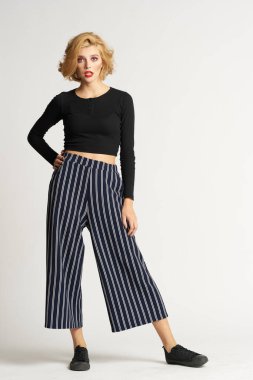 Siyah kazaklı, çizgili pantolonlu, güzel bir kadın. Moda kıyafetleri arka planda.