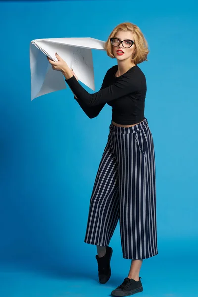 Hübsche Frau modische Kleidung großes Papierflugzeug in der Hand blauer Hintergrund — Stockfoto