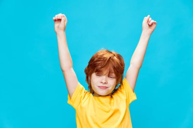 Kollarını kaldırıp sarı tişörtlü mutlu, kızıl saçlı bir genç. 