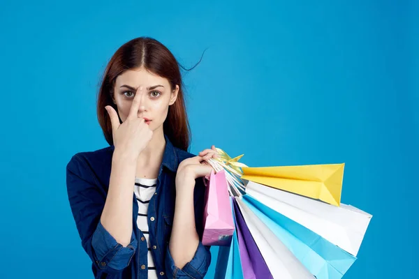Mujer de moda es ir de compras con paquetes en un fondo azul en una camiseta a rayas y chaqueta, gafas en la cara —  Fotos de Stock