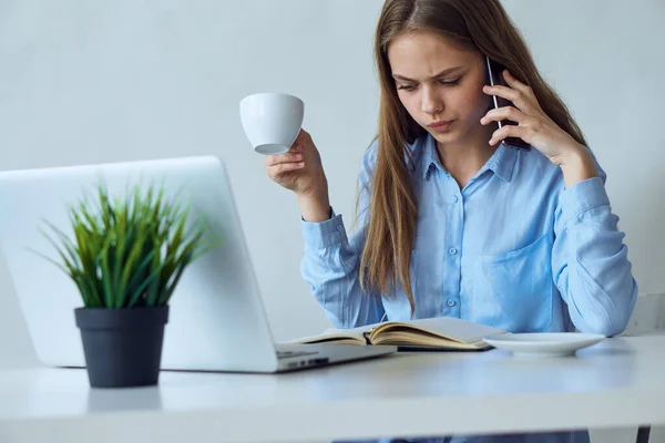 Zakelijke vrouw in een blauw shirt aan het bureau communiceert op de telefoon laptop kantoor kopje koffie — Stockfoto