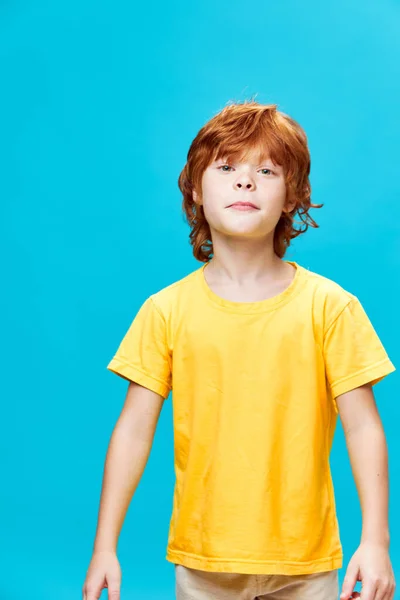 Sorgligt barn i gula T-shirts med rött hår på en blå bakgrund — Stockfoto