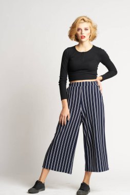 Siyah kazaklı, çizgili pantolonlu, güzel bir kadın. Moda kıyafetleri arka planda.