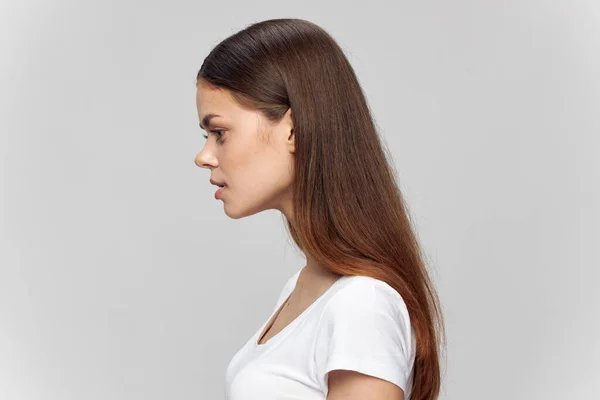 Brunette vrouw in een wit T-shirt op een lichte achtergrond bekijk close-up — Stockfoto