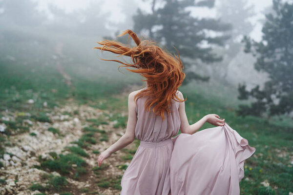 Red-haired woman in dress on nature fog travel fresh air back view. High quality photo