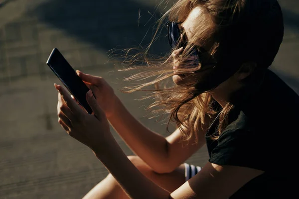 Mujer en la calle con un teléfono en la mano gafas de sol de aire fresco — Foto de Stock