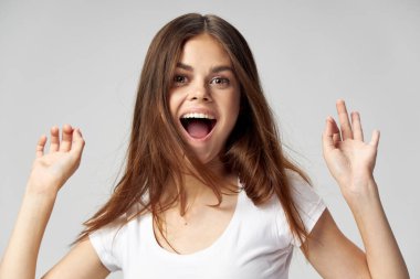 Beyaz tişörtlü, ağzı açık, elleri titreyen bir kadın. 