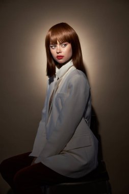 Elleriyle jestler yapan açık renk ceketli, kendine güvenen bir kadın. 