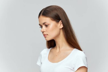 Beyaz tişörtlü esmer kadın. Arka planda açık renk bir model. 