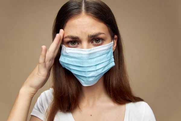 Красивая женщина в медицинской маске держит руку возле лица на бежевом фоне — стоковое фото