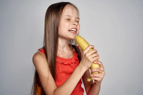 Κοριτσάκι με γυαλιά και κόκκινο φόρεμα με μπανάνα στα χέρια. — Φωτογραφία Αρχείου