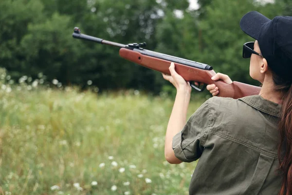 Mulher no exterior segurando uma arma perto de sua cabeça vista caça folhas verdes — Fotografia de Stock