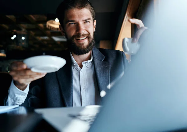 Homme d'affaires assis dans un café avec une tasse de café dans ses mains devant un ordinateur portable communication technologique — Photo