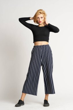 Siyah kazaklı, çizgili pantolonlu, güzel bir kadın. Moda kıyafetleri arka planda.