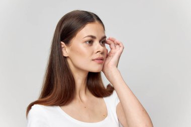 Beyaz tişörtlü esmer, izole edilmiş arka plan eliyle yüzüne dokunuyor ve boşluğu kopyalamaya doğru bakıyor.