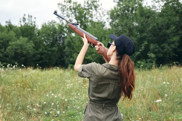 Mujer al aire libre sosteniendo un arma hasta mono verde caza estilo de vida gorra negra — Foto de Stock