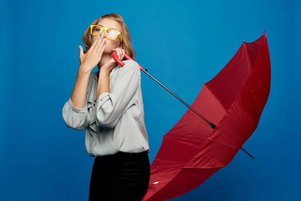 薄いシャツと黄色の眼鏡の青い背景に赤い傘を持つ女性 — ストック写真