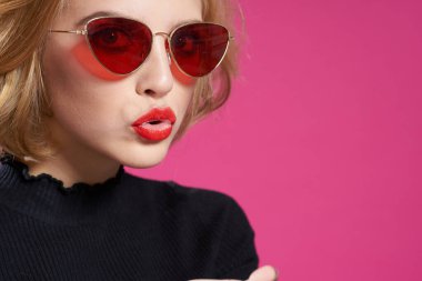 Koyu renk gözlüklü, parlak makyajlı, siyah ceketli, yakın plan pembe arka planlı güzel bir kadın.