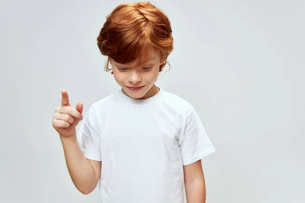 Roodharige jongen kijkt naar beneden en toont zijn wijsvinger omhoog Kopieer ruimte — Stockfoto