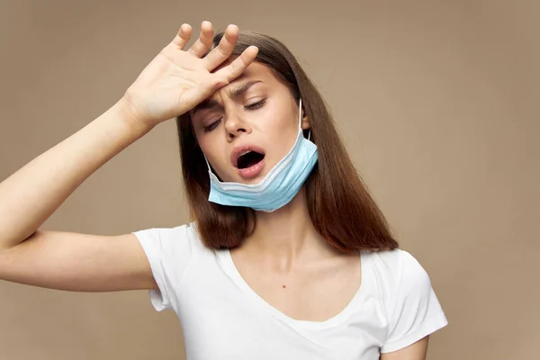 Mujer cansada con máscara médica en la barbilla toca su cabeza — Foto de Stock
