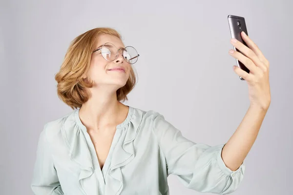 Mujeres con un teléfono móvil en sus manos toman fotos de sí mismas en una camisa sobre un fondo claro — Foto de Stock