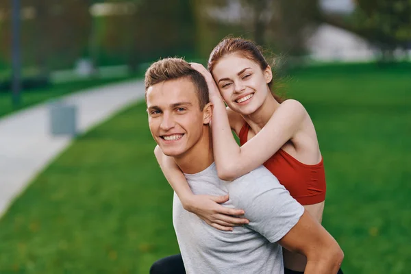 Щаслива жінка в червоній футболці на плечах чоловіка в літньому парку на природі — стокове фото