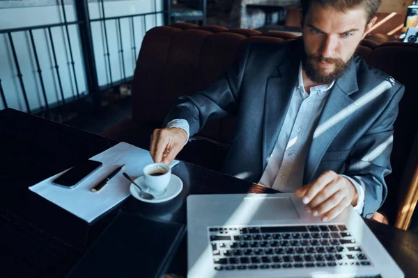 Uomo d'affari seduto in un caffè con una tazza di caffè tra le mani di fronte a una comunicazione tecnologia portatile — Foto Stock