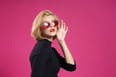 Koyu renk gözlüklü, parlak makyajlı, siyah ceketli, yakın plan pembe arka planlı güzel bir kadın.