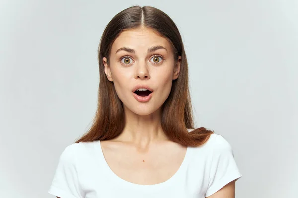 A surprised woman with an open mouth in a white t-shirt looks ahead