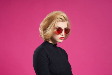 Koyu renk gözlüklü, parlak makyajlı, siyah ceketli, yakın plan pembe arka planlı güzel bir kadın.