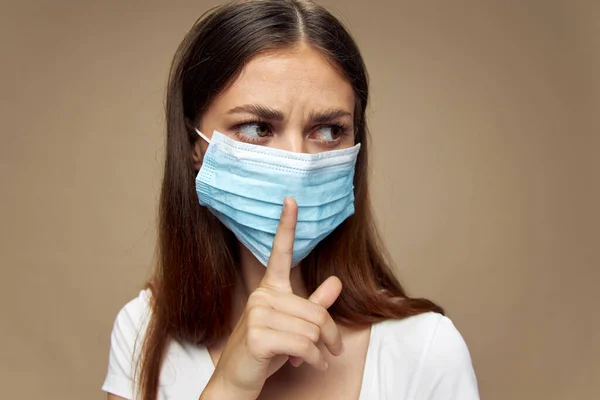 Una ragazza con una maschera medica tiene un dito davanti al viso e guarda di lato — Foto Stock