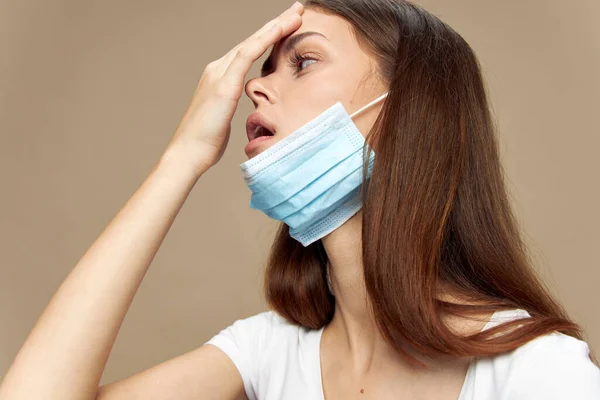 Femme touche sa tête avec la main et un masque médical sur un visage de t-shirt blanc — Photo